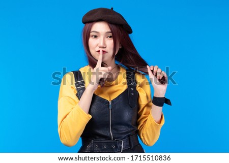 Image of feeling smile and happy. Cheerful young asian woman with red long hair in casual shirt, leather vest and hat on blue background. Female face expressions, smiling and emotions concept.