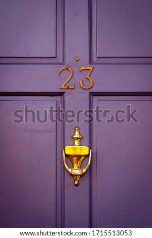 House number 23 on a purple wooden front door with golden door knocker