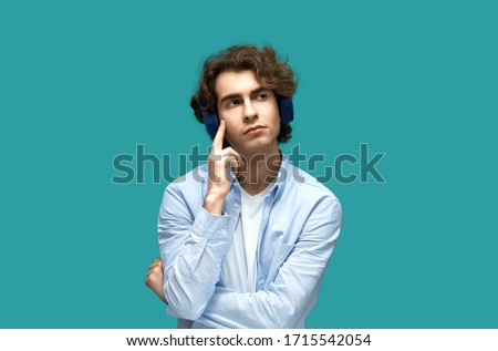 Portrait of a young beautiful man wearing white t-shirt and blue shirt in blue headphones. Thought holding a forefinger at his temple