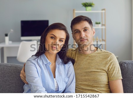 A couple in a serious emotional mood with problems looks at the camera while sitting on the couch.