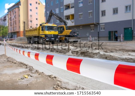 Red and white safety tape at the entrance of construction site with truck and excavator in the background