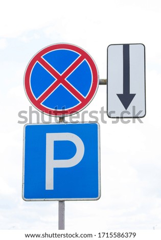 Three road signs: parking, one way, stopping prohibited, direct traffic. Signs on one pillar. Vertical photo.