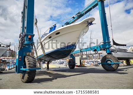 Boat-lift is lifting and transporting a boat in a boatyard for maintenance, repairs and cleaning in a sunny day Royalty-Free Stock Photo #1715588581