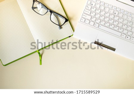 White laptop with keyboard, black glasses, an opened green notebook on a yellow background, composition. Flat lay and top view photo