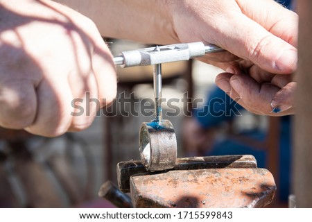 Man doing a tap in an iron ring by rotating a threat cutting tool and using petroleum jelly, with both hands, outdoor, landscape picture