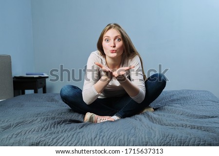 Young beautiful woman showing lips with kiss, female looks at camera, gesture to you, sitting at home in bed. Emotion love, happiness, joy, young people concept