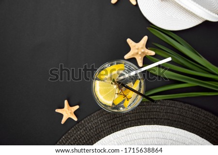 Colorful summer female fashion outfit. Black and white straw hat, flip flops, palm branches, leminade on black background, top view, flat lat. Summer fashion, holiday concept, travel or vacation