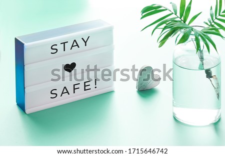 Lightbox with text "Stay safe", glass bottle with palm leaf and wooden heart. Wishing well to friends and family during quarantine and social distancing due to coronavirus pneumonia across the globe