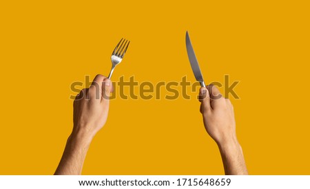 Close up of young guy holding knife and fork on orange background, panorama Royalty-Free Stock Photo #1715648659