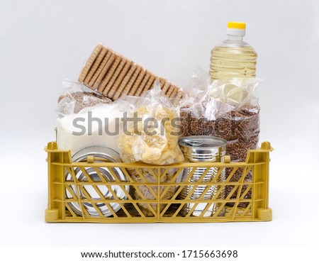 Products in packages of sugar, buckwheat, pasta, oil in a bottle in a box are on a white background. The concept of delivery of necessary products during quarantine and self-isolation. Isolate Royalty-Free Stock Photo #1715663698