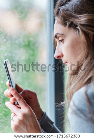 Woman taking a picture of the rain through the window of her house