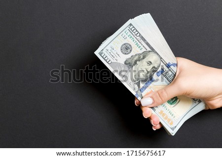 Top view of female hand giving one hundred dollar bills on colorful background. Charity and donation concept with copy space.