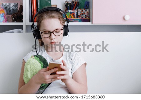 Girl teenager in glasses listens to music on the headphones of a smartphone. Home furnishings. Selective focus. Blur background.