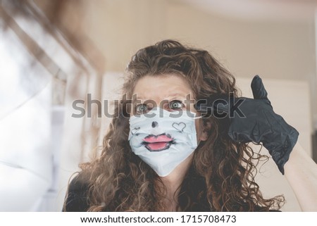 young woman wearing a painted surgical mask is doing the "shoot yourself" gesture