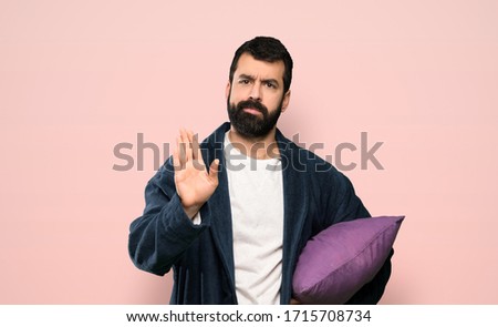 Man with beard in pajamas making stop gesture over isolated pink background