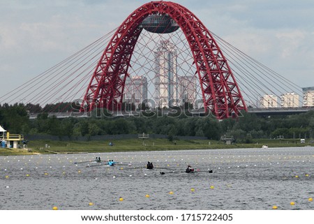Athletes on boats float along the canal against the background of the bridge and the residential area of the city.