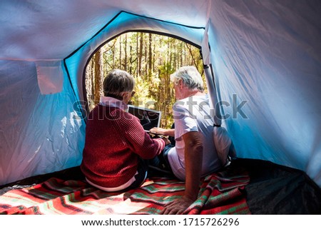 Elderly alternative travel lifestyle for old senior people sit down inside a tent with modern device - concept of youthful and no limit age to enjoy the world and life