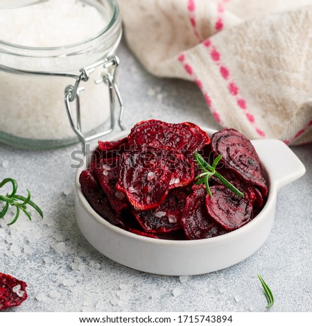 Healthy organic Purple Baked Beet (beetroot) Chips with olive oil, large Sea Salt and rosemary in a white bowl on a grey concrete background. Dietary useful snack. Selective focus, square picture