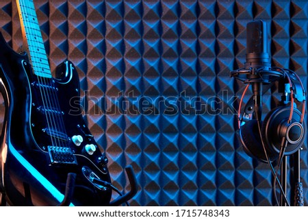 Musician setup. Professional studio condenser microphone with professional headphones and electric guitar, on acoustic foam panel background