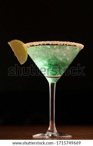 green cocktail in a martini glass rim covered with salt. with a slice of lime. close-up on a black background. macro