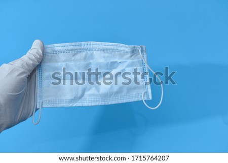 Doctors wear white gloves to prevent germs and catch masks to be ready to be worn at work.Over blue background.Protective raspiratory mask for spreading virus.Closeup,copy space, top view.
