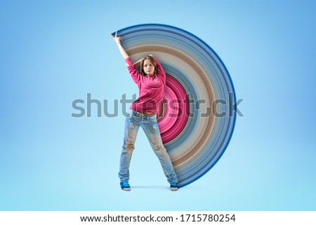 Young girl in pink hoodie and blue ripped jeans, standing with one arm raised and the other arm behind head, with pixel stretch effect on light blue background. Dancing. Creativity. Street fashion.