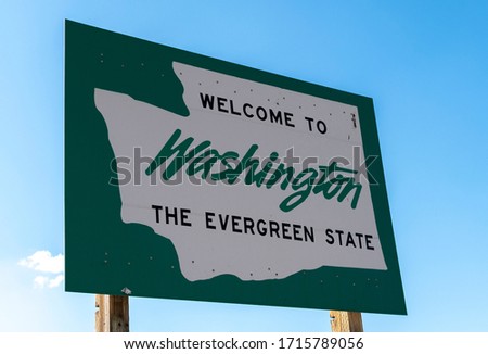A roadside sign with welcome to Washington State, the evergreen state written on it with a blue sky behind.