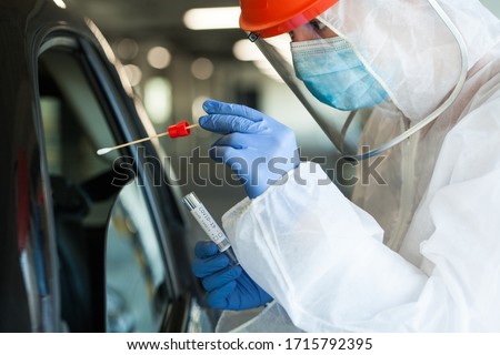 Medical worker in personal protective equipment swabbing a person in a car drive through Coronavirus COVID-19 mobile testing center,oral and nasal specimen collection procedure,health and safety  Royalty-Free Stock Photo #1715792395