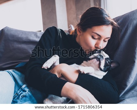 Beautiful young woman sitting on a sofa kissing and cuddling a dog.Young woman playing with her dog at home