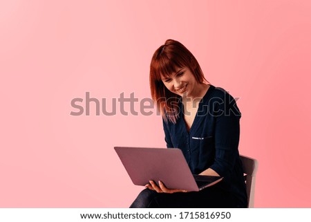 Woman with laptop computer sitting on the chair, isolated on pink background