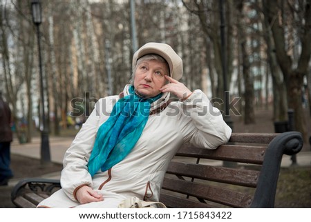 An elegantly dressed old woman is sitting on a bench in an alley in the Park . Active longevity.