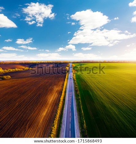 Aerial photography of rural road passing through agricultural land and cultivated fields. Top view drone shot. Agricultural area of Ukraine, Europe. Concept of agrarian industry. Beauty of earth.