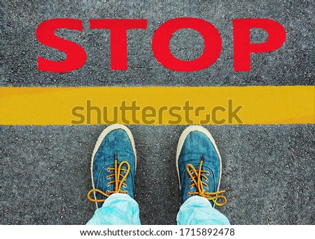 Women's feet in sneakers stand at the line with the inscription "stop".