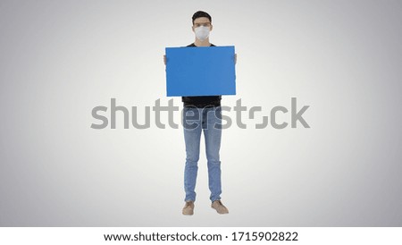 Student in medical mask holding blank placard on gradient background.