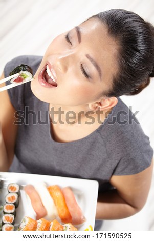 Beautiful young woman eating sushi. Shallow depth of field, focus is on the eyes. 