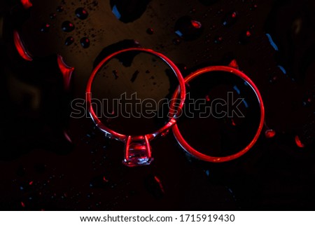 Wedding gold rings in blue-red neon light on a dark background with water drops