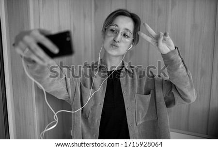 European girl using a mobile phone communicates with friends in an online chat. a smiling girl with glasses communicates in an online chat via video communication. black and white photo