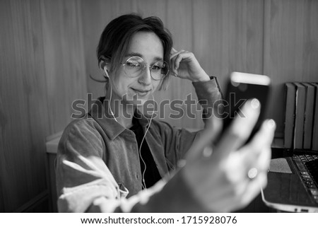 European girl using a mobile phone communicates with friends in an online chat. a smiling girl with glasses communicates in an online chat via video communication. black and white photo