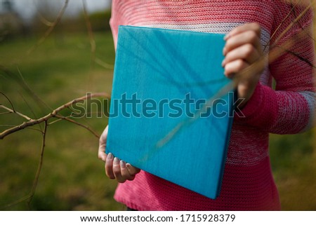 Girl in pink sweater holding photobook or photoalbum with leather turquoise cover and wooden texture.