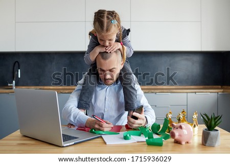 Father Working from home on laptop during quarantine. Little child girl make noise and distracts father from work on the kitchen office Royalty-Free Stock Photo #1715936029