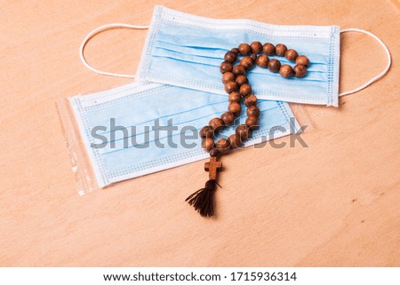 Blue medical masks and christian rosary with catholic cross on a wooden table background.