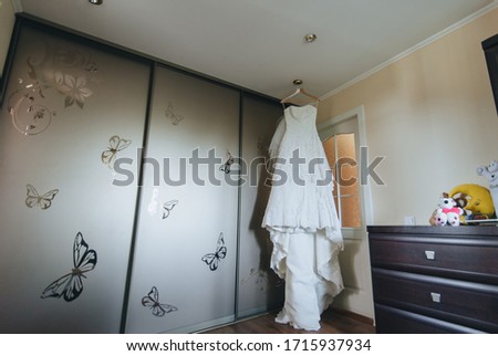 Wedding white long dress hanging on a hanger against the background of the wardrobe in a beautiful interior. Photography, concept.