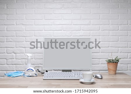 Blank screen computer monitor on working desk with coffee cup, vase of cactus and corona protection