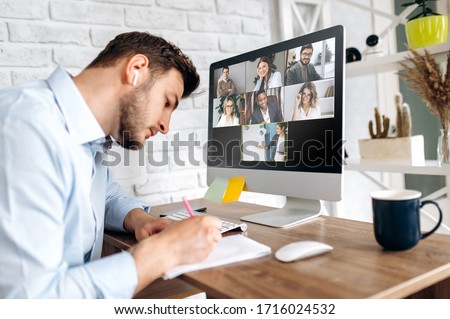 Online training. Young guy learns online by video conference in zoom app. On the screen, the teacher tells the information to him and other participants in the conference Royalty-Free Stock Photo #1716024532