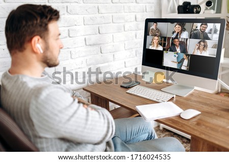 Online training. Young guy learns online by video conference in zoom app. On the screen, the teacher tells the information to him and other participants in the conference Royalty-Free Stock Photo #1716024535