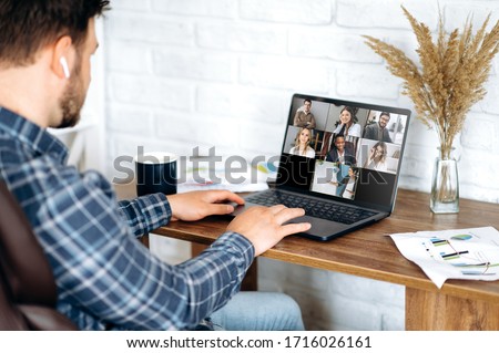 Video call. Online business meeting in video conference in the zoom app. A young attractive guy communicates with his colleagues on a video call using a laptop. Distant work at home Royalty-Free Stock Photo #1716026161