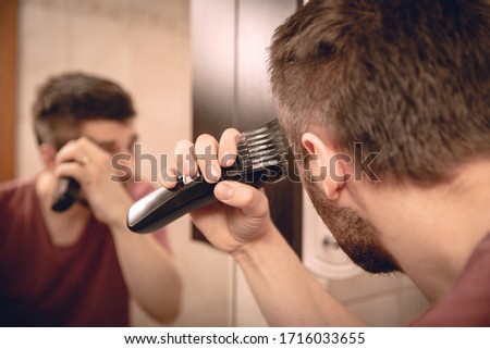 A man cuts his hair on his head with an electric razor  Royalty-Free Stock Photo #1716033655