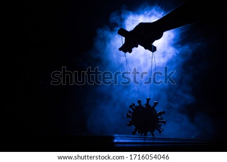 Creative concept of manipulation with coronavirus. Hand holds strings for manipulation. The hand controls the Covid19 miniature with strings on a dark foggy background. Selective focus
