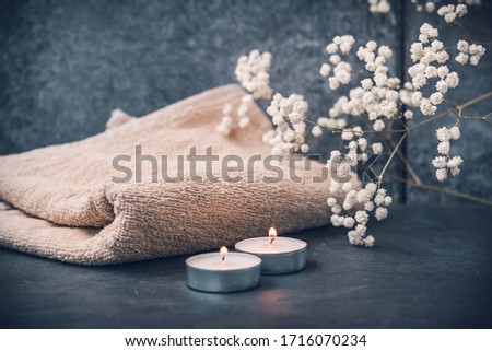 Light fluffy beige towels with spa paraphernalia, candles and flowers on a dark gray background