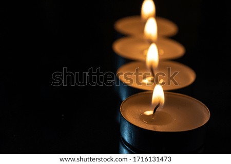 four candles lined up with dark background showing the light of the fire and the reflection in the mirror